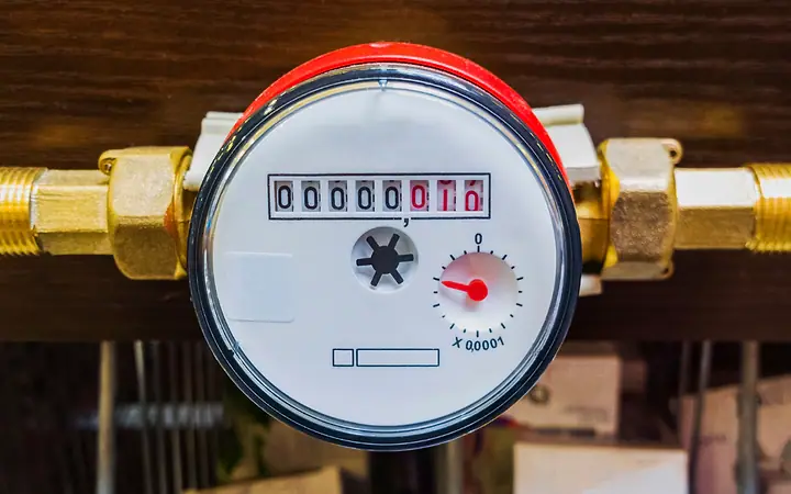 Hidrômetro com mostrador vermelho instalado entre conexões de latão